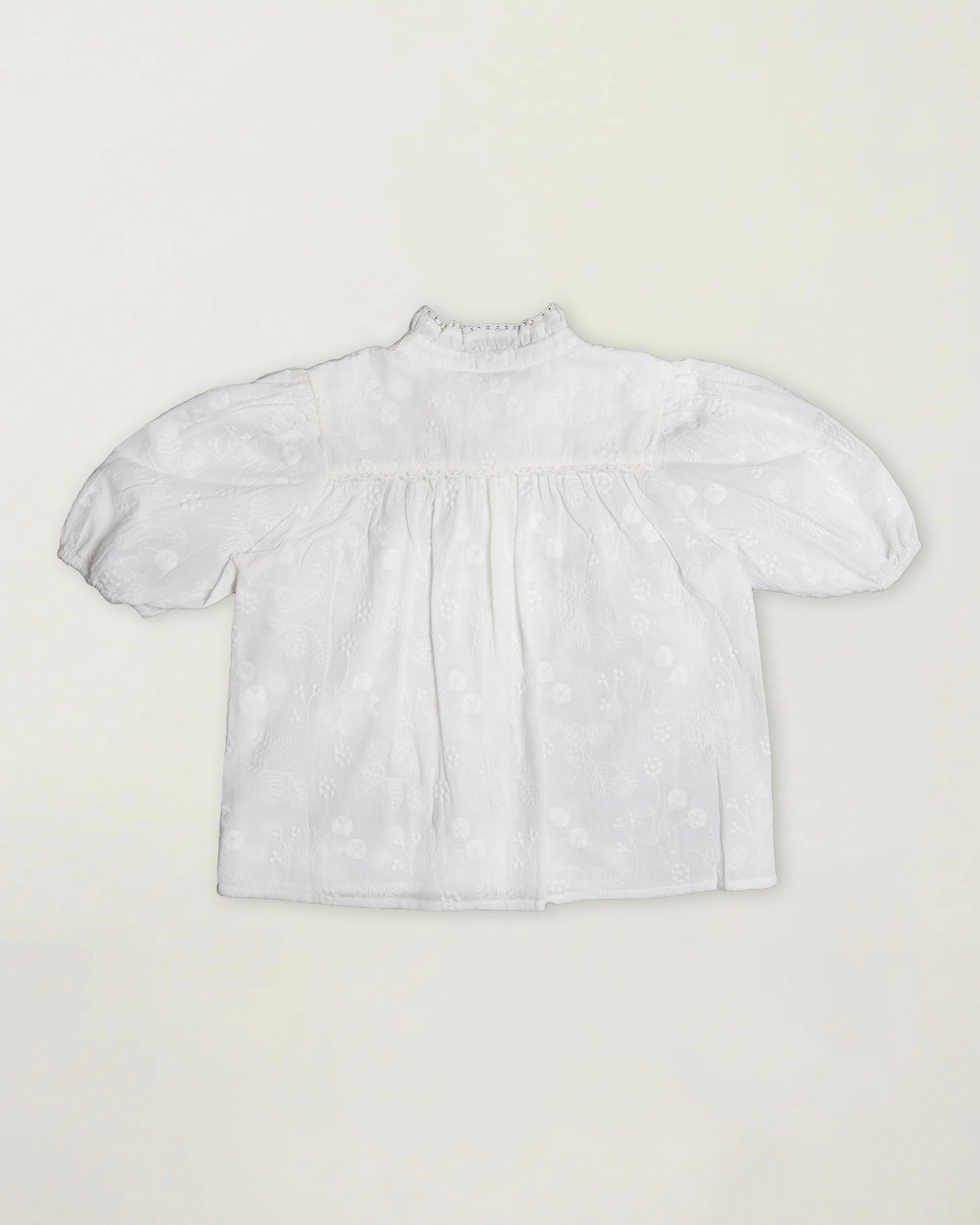 Early Sunday, Coco Blouse in Ivory color, made from all over embroidery fabric, featuring Puff sleeves, ruffled neckline and placket, shown in a back flat-lay view