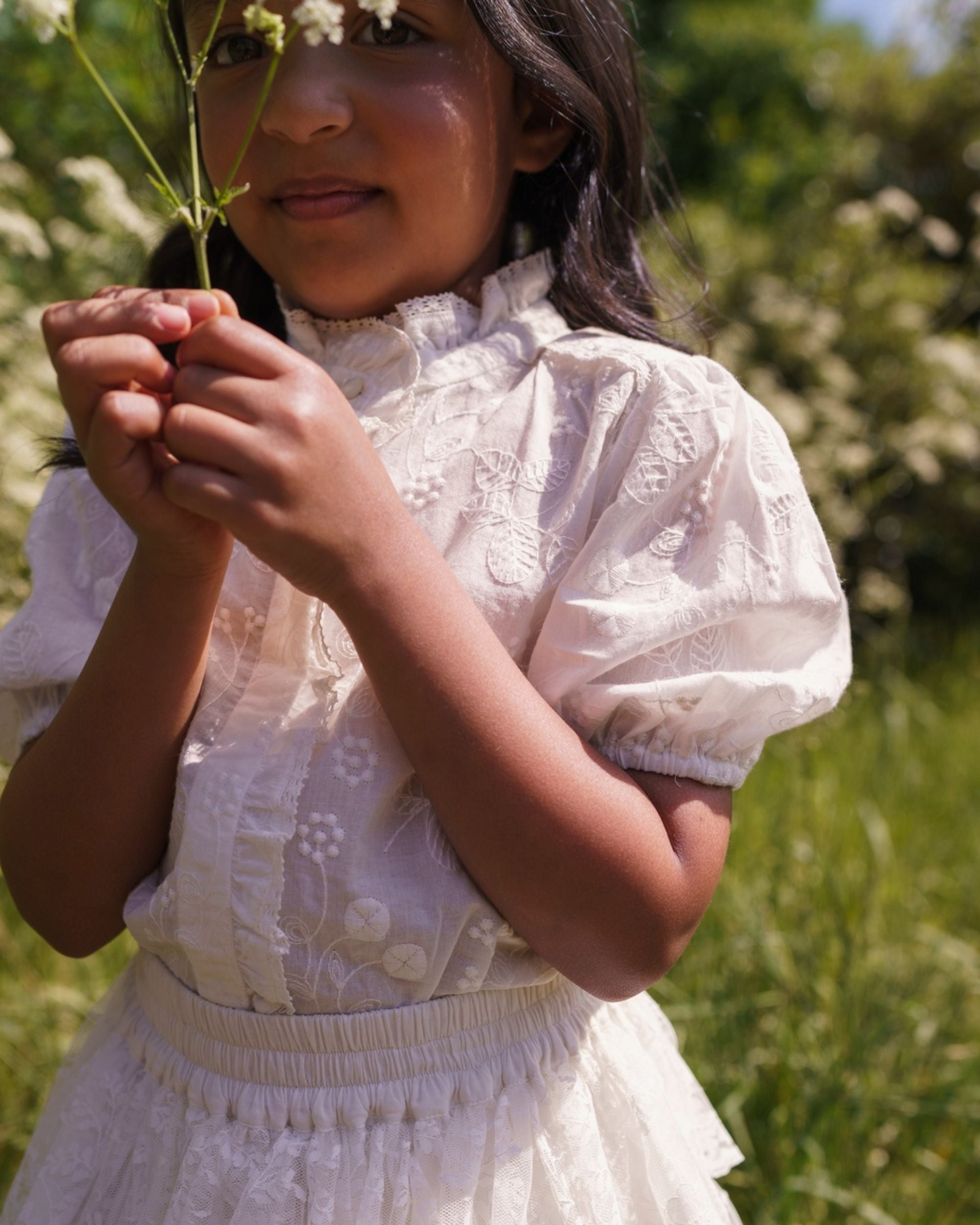 Early Sunday, Coco Blouse in Ivory color, made from all over embroidery fabric, featuring Puff sleeves, ruffled neckline and placket, shown in a close up shot of model wearing it