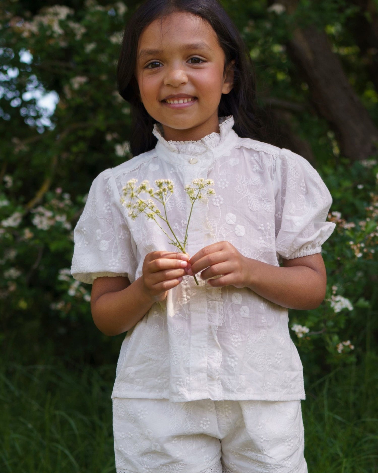 Early Sunday, Coco Blouse in Ivory color, made from all over embroidery fabric, featuring Puff sleeves, ruffled neckline and placket, shown in a front view of model wearing it
