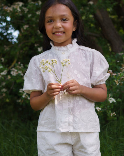 Early Sunday, Coco Blouse in Ivory color, made from all over embroidery fabric, featuring Puff sleeves, ruffled neckline and placket, shown in a front view of model wearing it