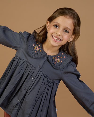 Early Sunday, Colette Blouse in Stormy Blue, made from Cotton Satin fabric, featuring relaxed fit, classic collar, and button-down front, shown in a close-up side view of a model wearing it