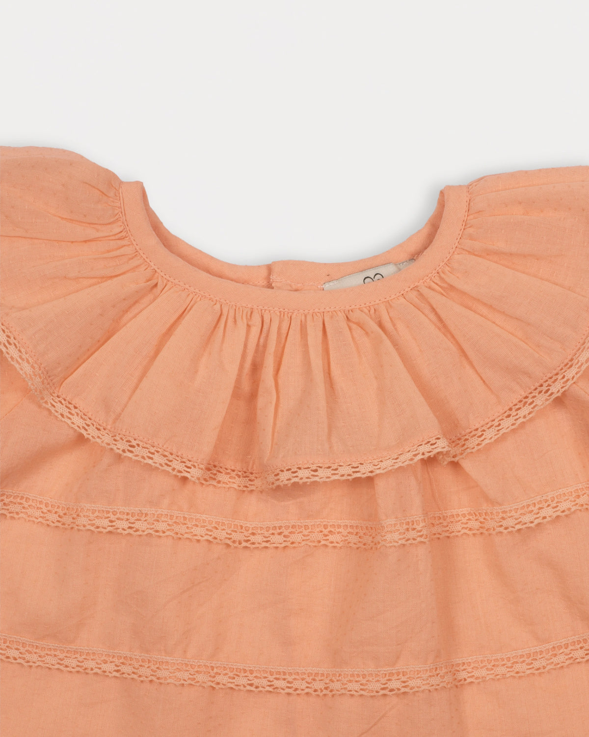 Early Sunday, Daisy Baby Blouse & Bloomer Set in Dusty Pink, made from Cotton Dobby Spot fabric, featuring a frilly neckline with detailed lace yoke & gathered sleeves, shown in a closeup flat-lay view