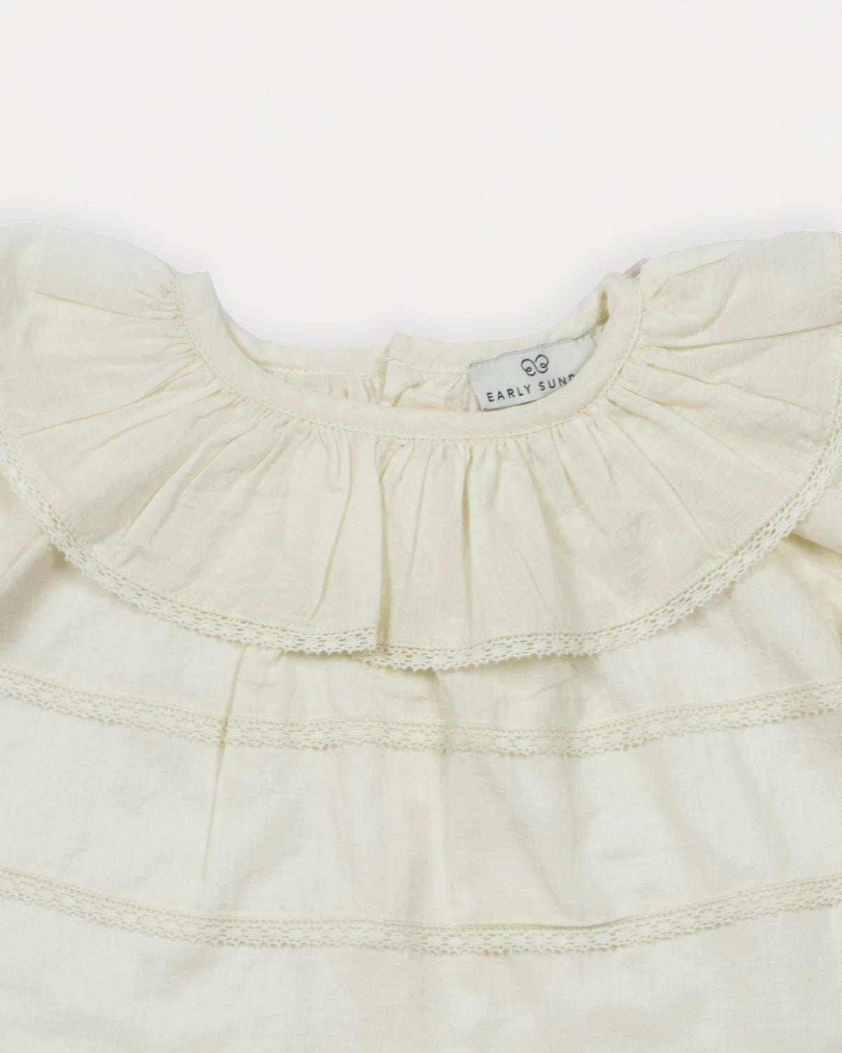 Early Sunday, Daisy Baby Blouse & Bloomer Set in Ivory, made from Cotton Dobby Spot fabric, featuring a frilly neckline with detailed lace yoke & gathered sleeves, shown in a closeup flat-lay view