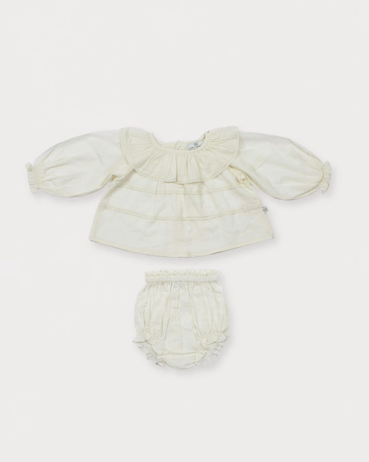 Early Sunday, Daisy Baby Blouse & Bloomer Set in Ivory, made from Cotton Dobby Spot fabric, featuring a frilly neckline & detailed lace yoke with matching bloomer, shown in a front flat-lay view