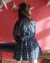 Early Sunday, Dawn Dress in Ditsy Bouquet Navy, made from Printed Cotton Satin fabric, featuring a soft flowing hem, shown in a back view of a model wearing it in a studio setting