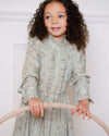 Early Sunday, Dawn Dress in Ditsy Bouquet Jade print, made from Printed Viscose Rayon Twill fabric, featuring Collar and sleeve cuffs trimmed with subtle ruffles for a nostalgic silhouette, shown in a close up shot of model wearing it