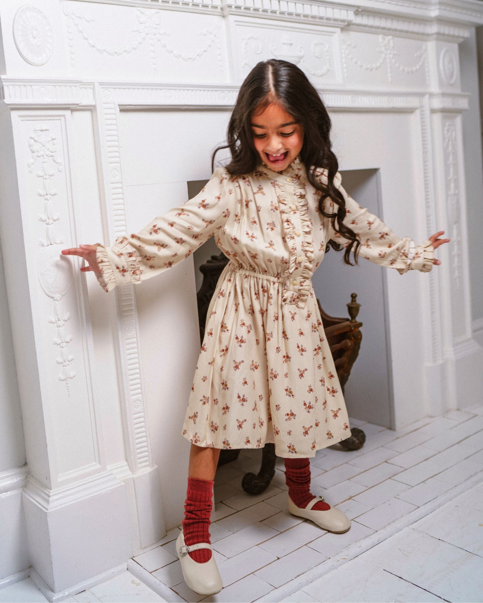 Early Sunday, Dawn Dress in Ditsy Bouquet Cream print, made from Printed Viscose Rayon Twill fabric, featuring Collar and sleeve cuffs trimmed with subtle ruffles for a nostalgic silhouette, shown in a front view of a model wearing it in a studio setting