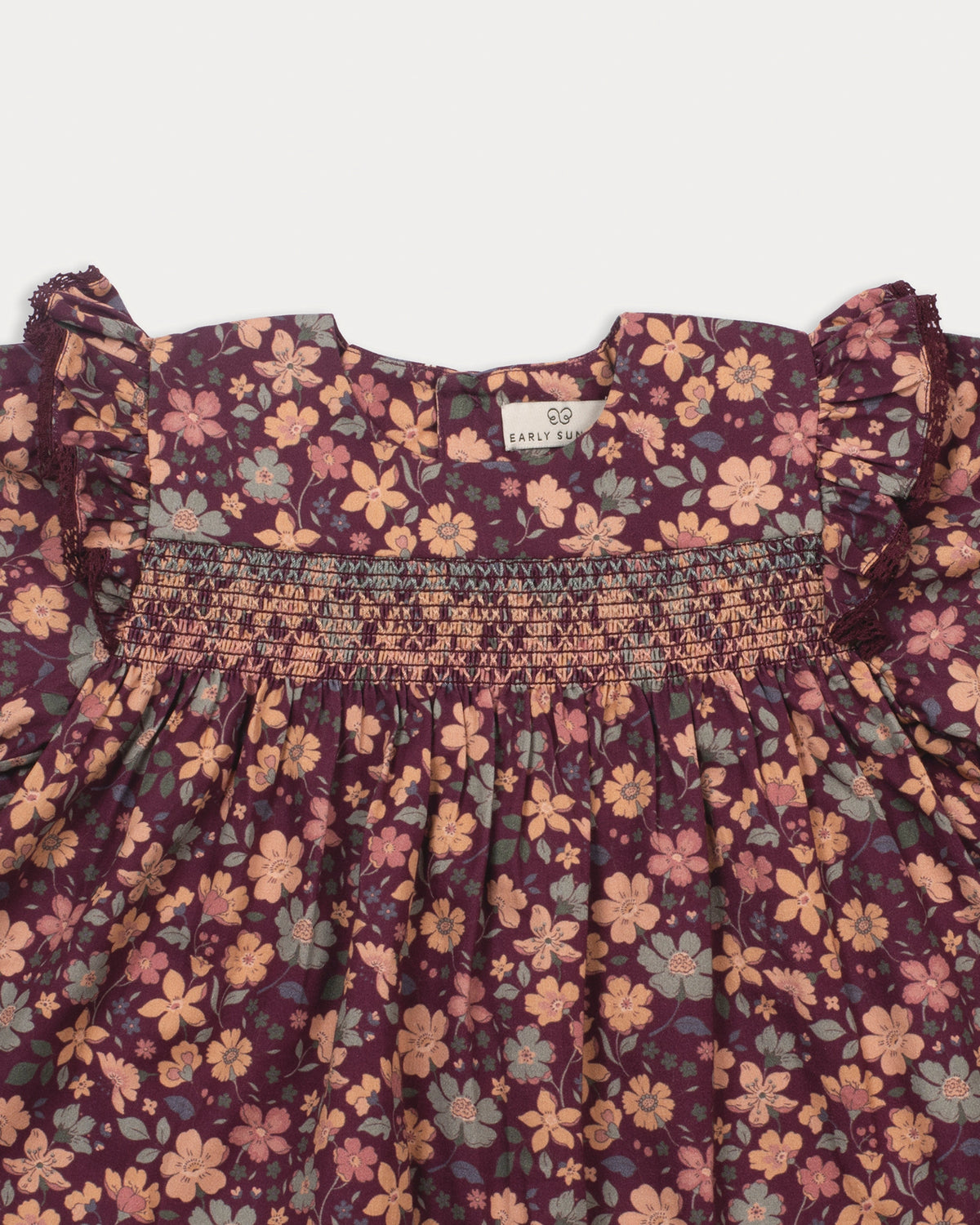 Early Sunday, Ellie Baby Dress & Bloomer Set in Garden Flowers Plum, made from Printed Cotton Satin fabric, featuring frilly sleeves across shoulder & smocked chest, shown in a closeup flat-lay view