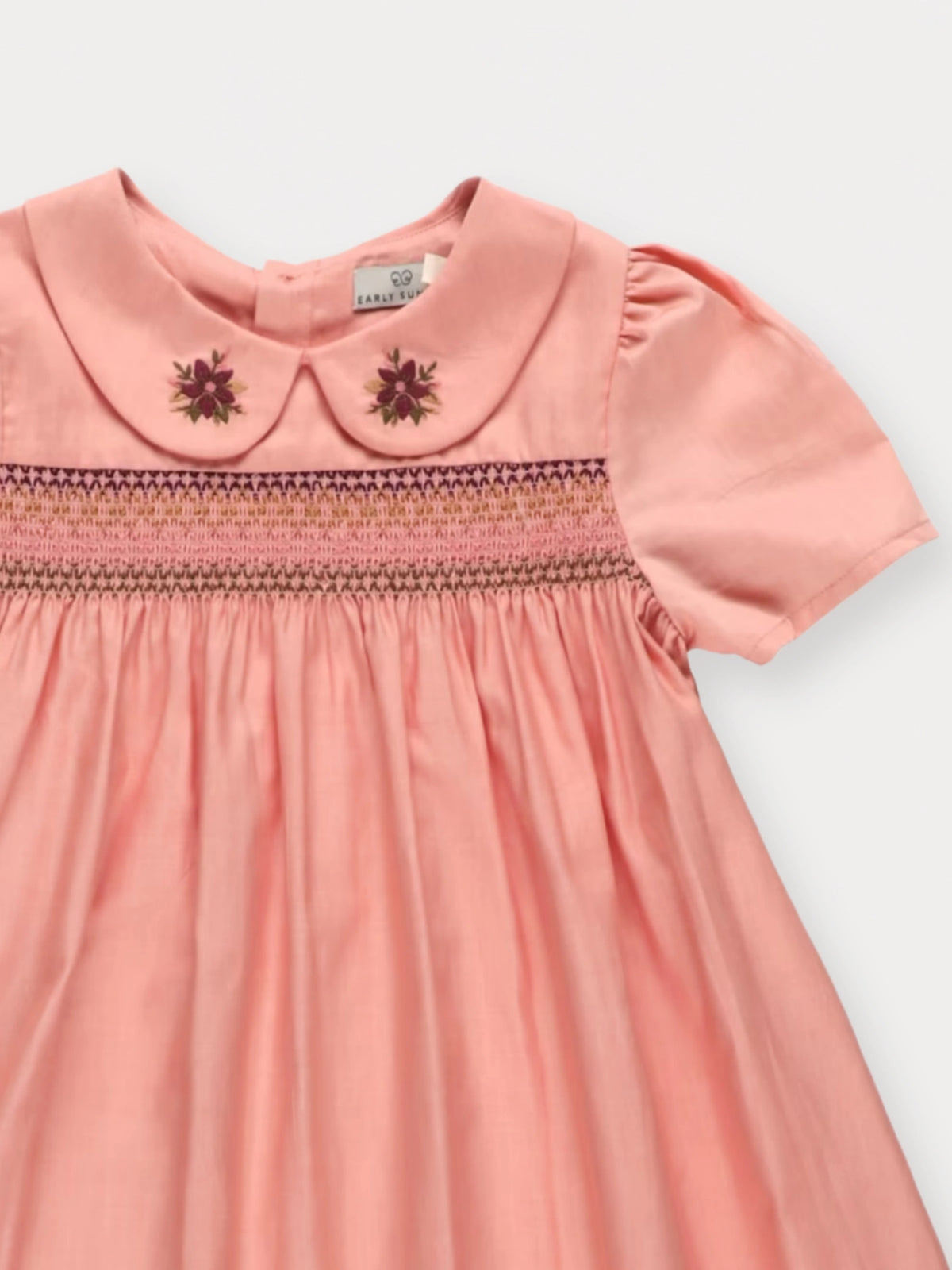 Early Sunday, Erika Dress in Blush Pink, made from Cotton Satin fabric, featuring a floral embroidery on a Peter Pan collar with a delicately smocked chest, shown in a closeup flat-lay view