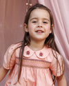 Early Sunday, Erika Dress in Blush Pink, made from Cotton Satin fabric, featuring a floral embroidery on a Peter Pan collar with a delicately smocked chest, shown in a close up shot of model wearing it