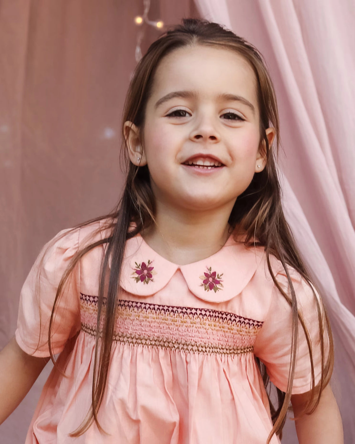 Early Sunday, Erika Dress in Blush Pink, made from Cotton Satin fabric, featuring a floral embroidery on a Peter Pan collar with a delicately smocked chest, shown in a close up shot of model wearing it