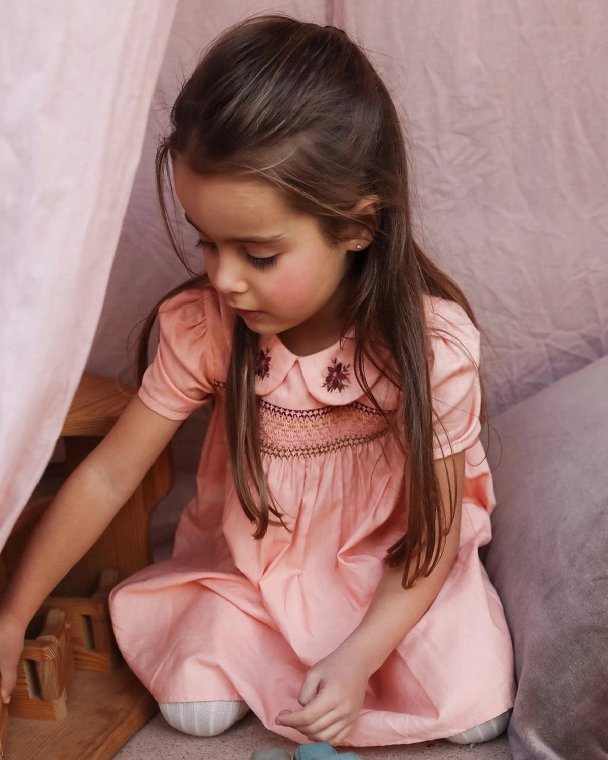 Early Sunday, Erika Dress in Blush Pink, made from Cotton Satin fabric, featuring a floral embroidery on a Peter Pan collar with a delicately smocked chest, shown in a front view of model playing outdoors