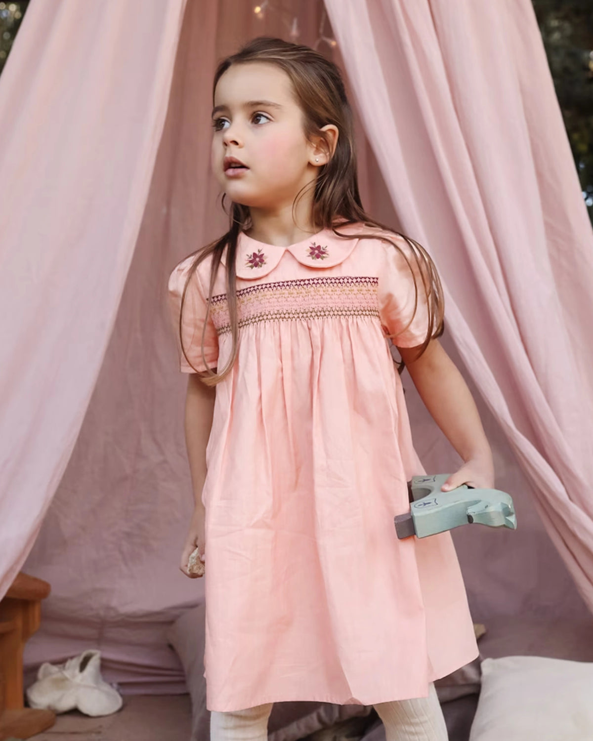 Early Sunday, Erika Dress in Blush Pink, made from Cotton Satin fabric, featuring a floral embroidery on a Peter Pan collar with a delicately smocked chest, shown in a front view of model wearing it