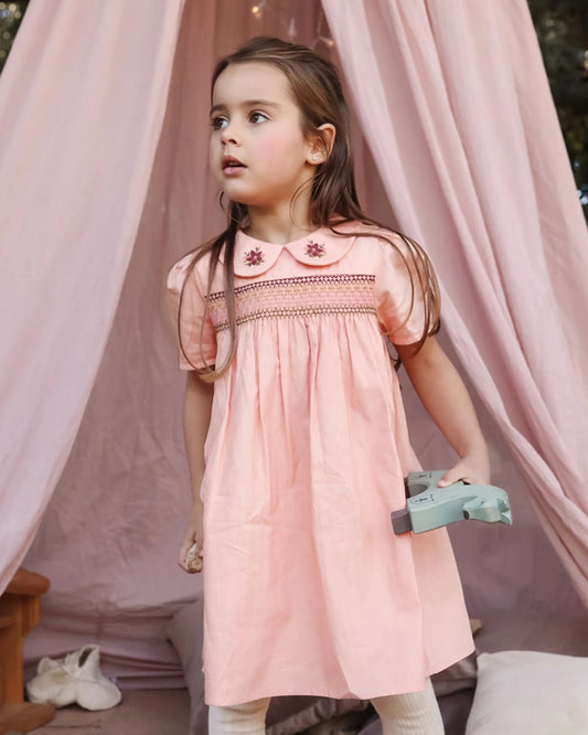Early Sunday, Erika Dress in Blush Pink, made from Cotton Satin fabric, featuring a floral embroidery on a Peter Pan collar with a delicately smocked chest, shown in a front view of model wearing it