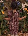 Early Sunday, Erika Dress in Plum, made from Printed Cotton Satin fabric, featuring a floral print with peter pan collar, shown in a back view of model wearing outdoors