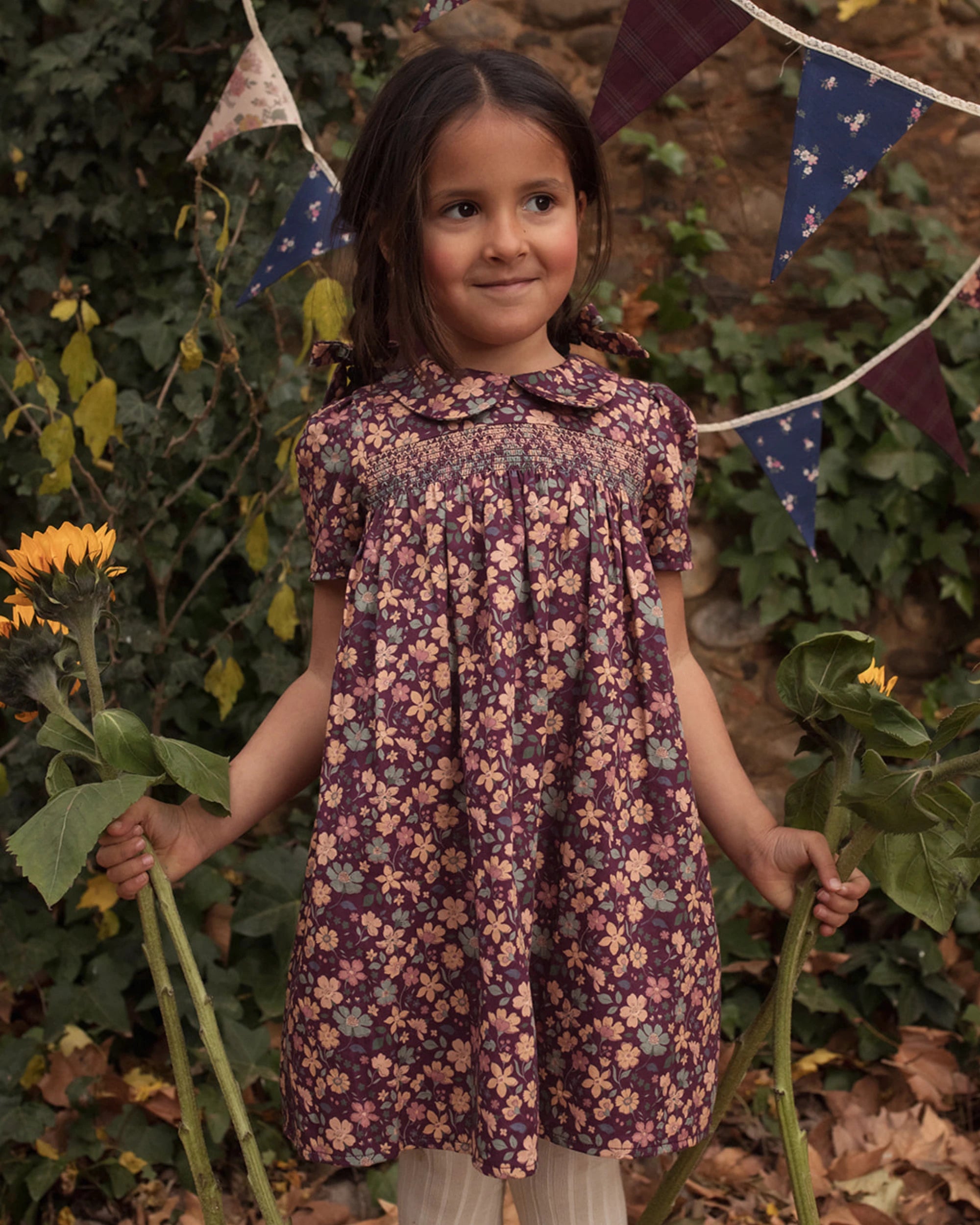 Early Sunday, Erika Dress in Plum, made from Printed Cotton Satin fabric, featuring a floral print with peter pan collar, shown in a front view of model wearing outdoors