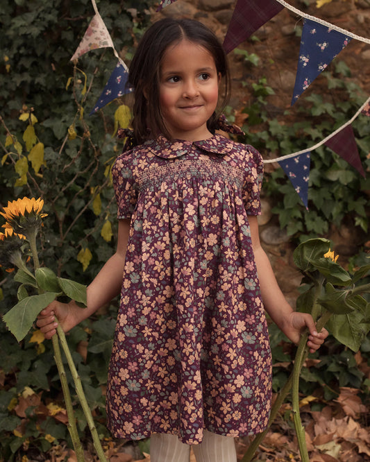 Early Sunday, Erika Dress in Plum, made from Printed Cotton Satin fabric, featuring a floral print with peter pan collar, shown in a front view of model wearing outdoors