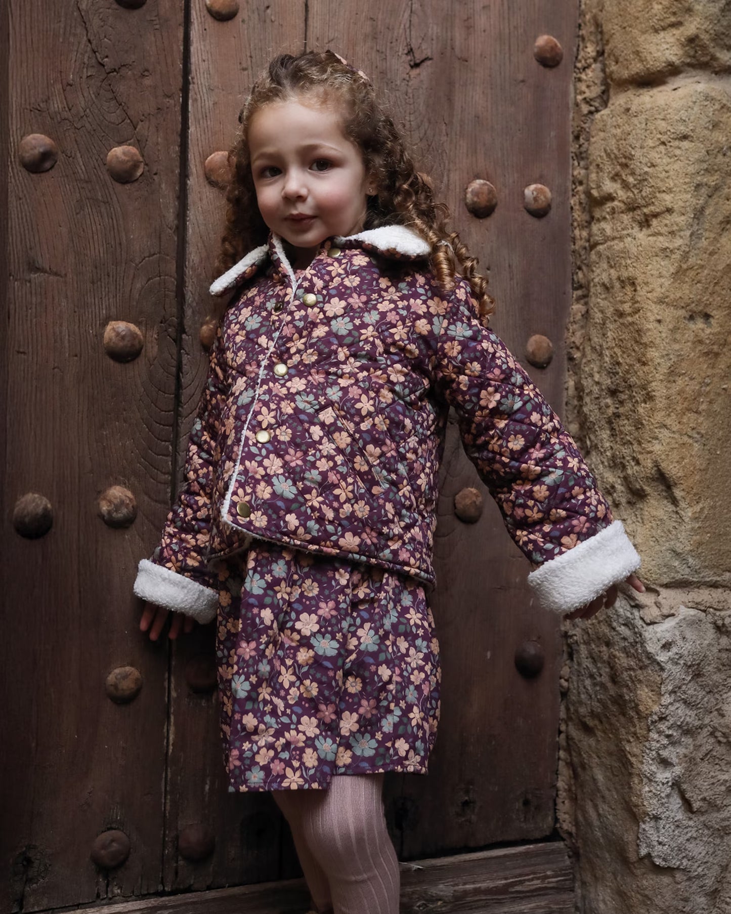 Early Sunday, Esmée Jacket in Garden Flowers Plum, made from Printed Cotton Satin fabric, featuring a quilted layer with delicate floral print and elegant detailing, shown in a front view of model wearing outdoors