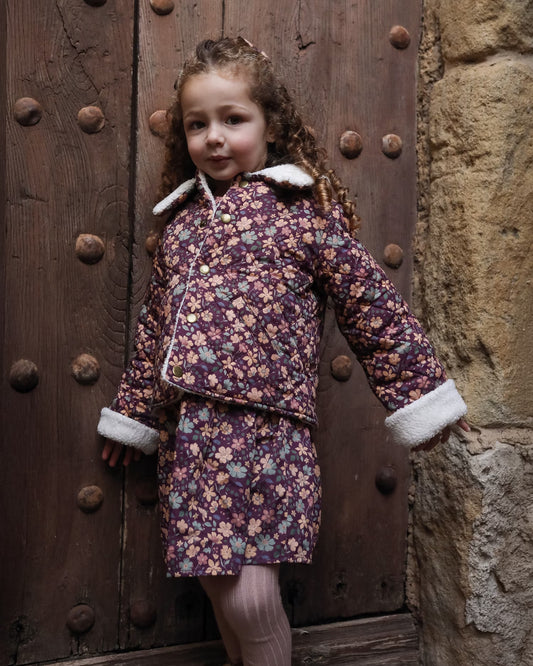 Early Sunday, Esmée Jacket in Garden Flowers Plum, made from Printed Cotton Satin fabric, featuring a quilted layer with delicate floral print and elegant detailing, shown in a front view of model wearing outdoors