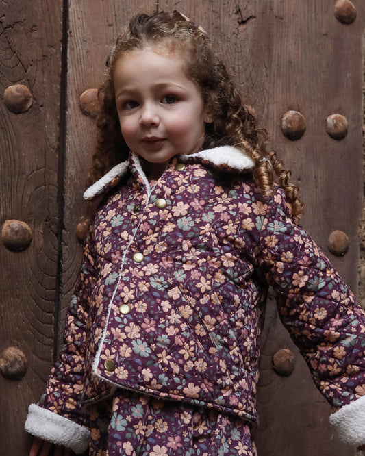 Early Sunday, Esmée Jacket in Garden Flowers Plum, made from Printed Cotton Satin fabric, featuring a quilted layer with delicate floral print and elegant detailing, shown in a front view of model wearing outdoors