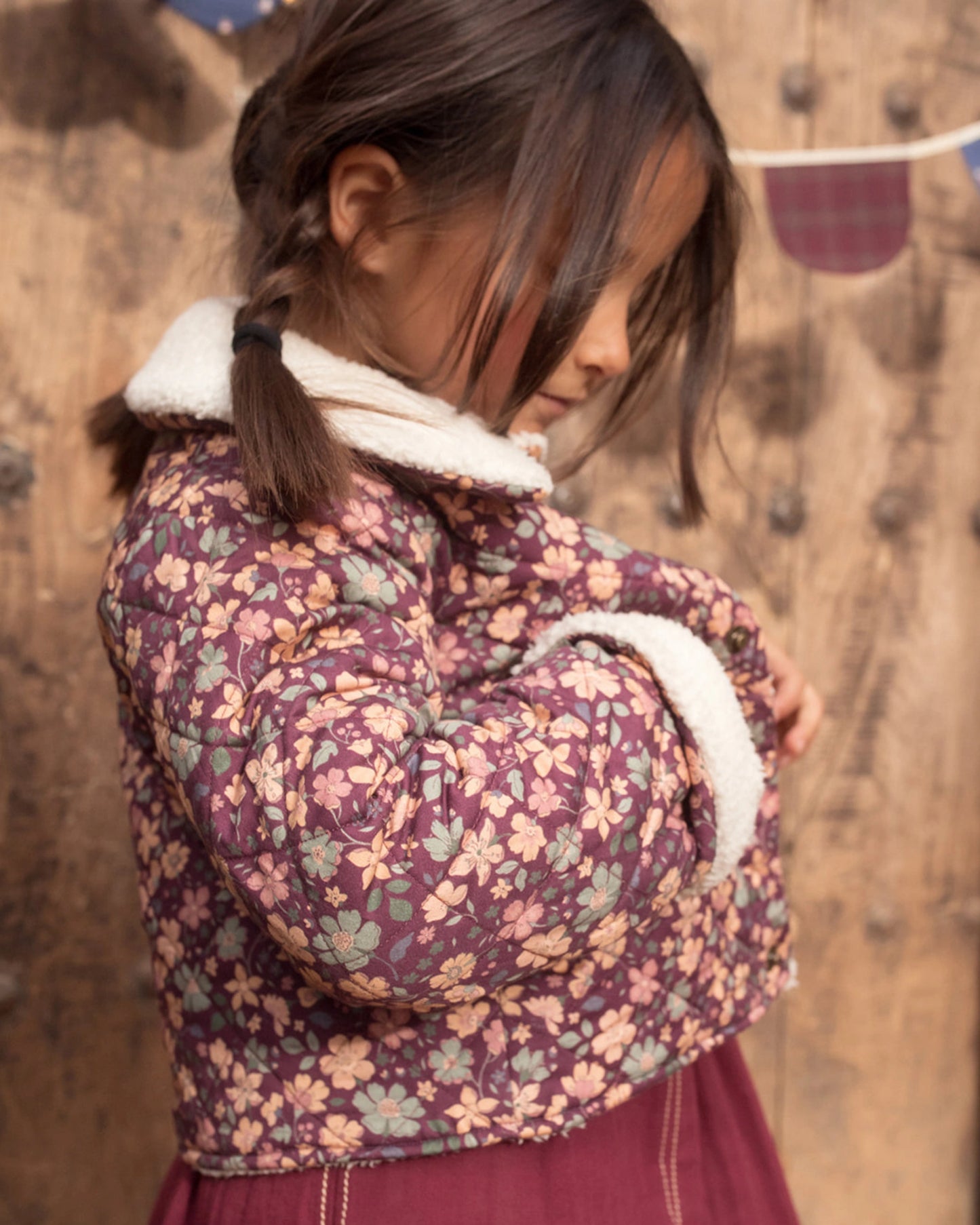Early Sunday, Esmée Jacket in Garden Flowers Plum, made from Printed Cotton Satin fabric, featuring a quilted layer with delicate floral print and elegant detailing, shown in a side view of model wearing outdoors