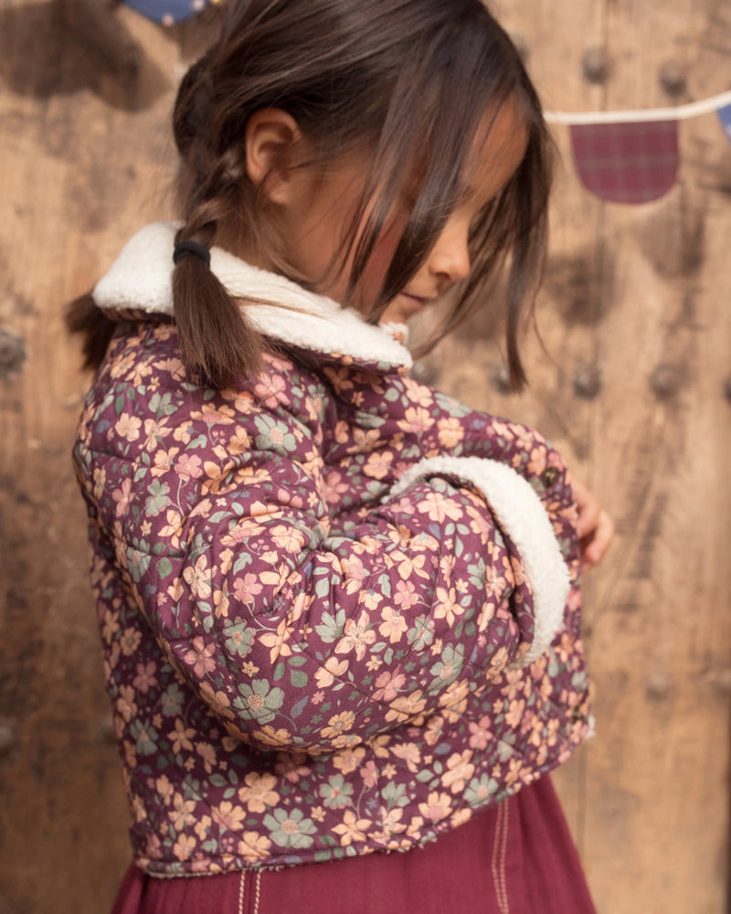 Early Sunday, Esmée Jacket in Garden Flowers Plum, made from Printed Cotton Satin fabric, featuring a quilted layer with delicate floral print and elegant detailing, shown in a side view of model wearing outdoors