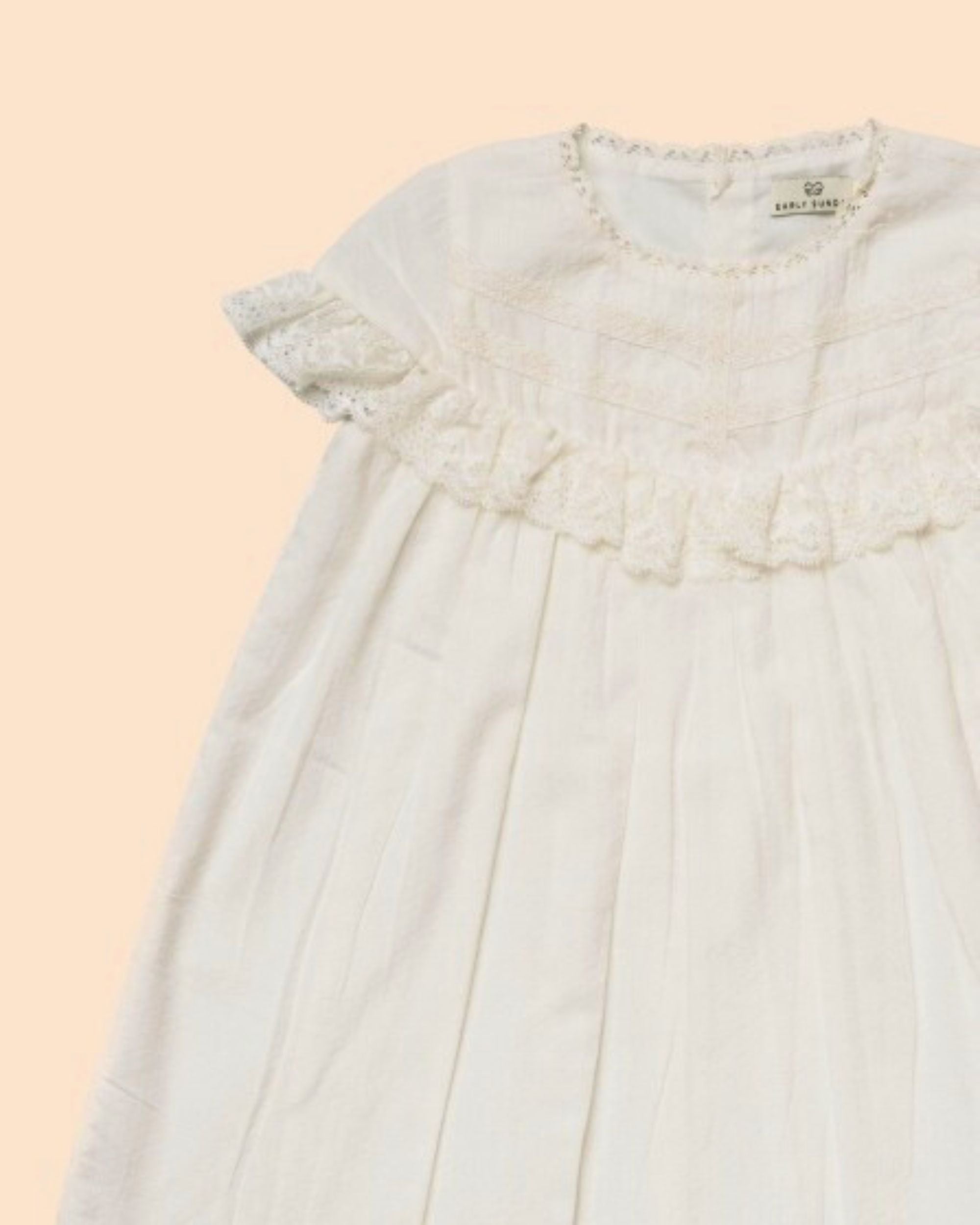 Early Sunday, Faustine Dress in Ivory color, made from 100% cotton swiss dobby tiny dots fabric, featuring Soft gathers with delicate ruffle accents, shown in a closeup flat-lay view