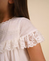 Early Sunday, Faustine Dress in Ivory color, made from 100% cotton swiss dobby tiny dots fabric, featuring Soft gathers with delicate ruffle accents, shown in a close up shot of model wearing it