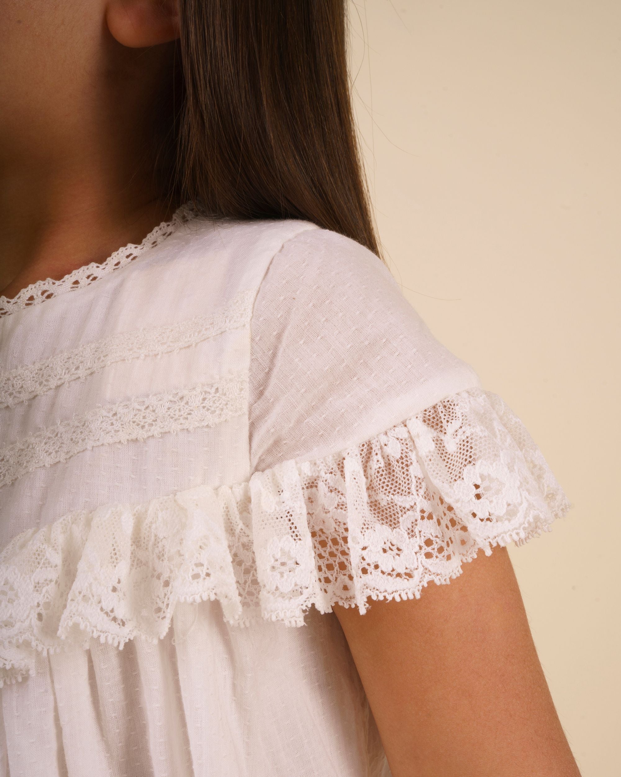 Early Sunday, Faustine Dress in Ivory color, made from 100% cotton swiss dobby tiny dots fabric, featuring Soft gathers with delicate ruffle accents, shown in a close up shot of model wearing it