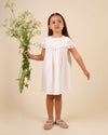 Early Sunday, Faustine Dress in Ivory color, made from 100% cotton swiss dobby tiny dots fabric, featuring Soft gathers with delicate ruffle accents, shown in a front view of model wearing it