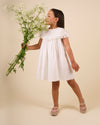 Early Sunday, Faustine Dress in Ivory color, made from 100% cotton swiss dobby tiny dots fabric, featuring Soft gathers with delicate ruffle accents, shown in a side view of model wearing it
