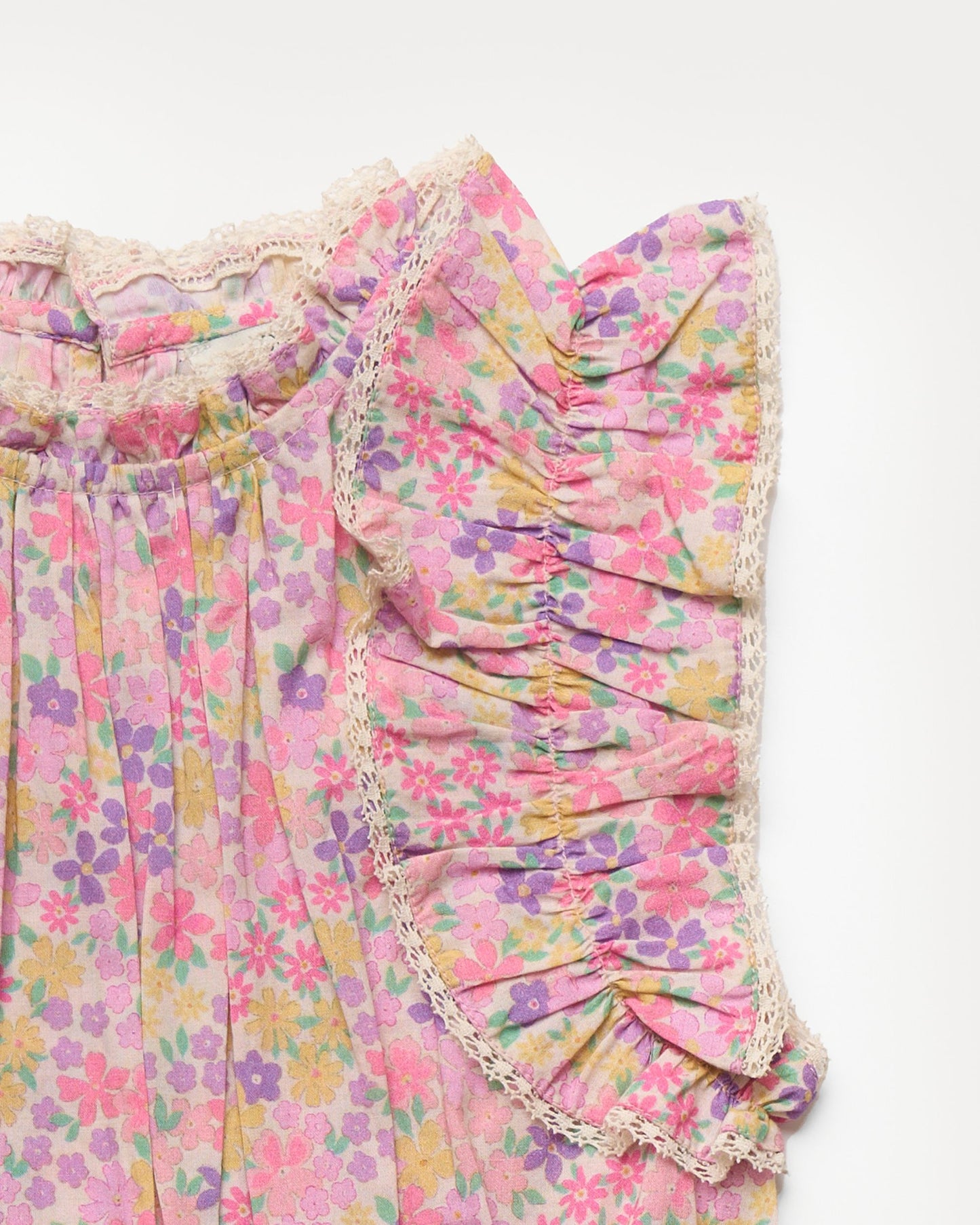 Early Sunday, Florence Dress in Emma Floral Purple color, made from printed cotton cambric fabric, featuring Ruffle detailing on the yoke and sleeves, lace accents, gathered waist with tassel tie, shown in a closeup flat-lay view