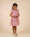 Early Sunday, Florence Dress in Emma Floral Purple color, made from printed cotton cambric fabric, featuring Ruffle detailing on the yoke and sleeves, lace accents, gathered waist with tassel tie, shown in a model standing facing front wearing