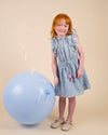 Early Sunday, Florence Dress in Tonal Floral Blue color, made from printed cotton tiny swiss dobby fabric, featuring Ruffle detailing on the yoke and sleeves, lace accents, gathered waist with tassel tie, shown in a front view of model wearing