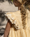 Early Sunday, Georgia Dress in Vanilla color, made from Cotton Dobby Swiss Dots fabric, featuring Flutter sleeves, pintuck detailing, and a flowy, gathered silhouette, shown in a back view of model wearing it