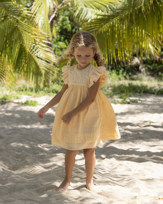 Early Sunday, Georgia Dress in Vanilla color, made from Cotton Dobby Swiss Dots fabric, featuring flutter sleeves, pintuck detailing, and a flowy, gathered silhouette, shown in a front view of model wearing it