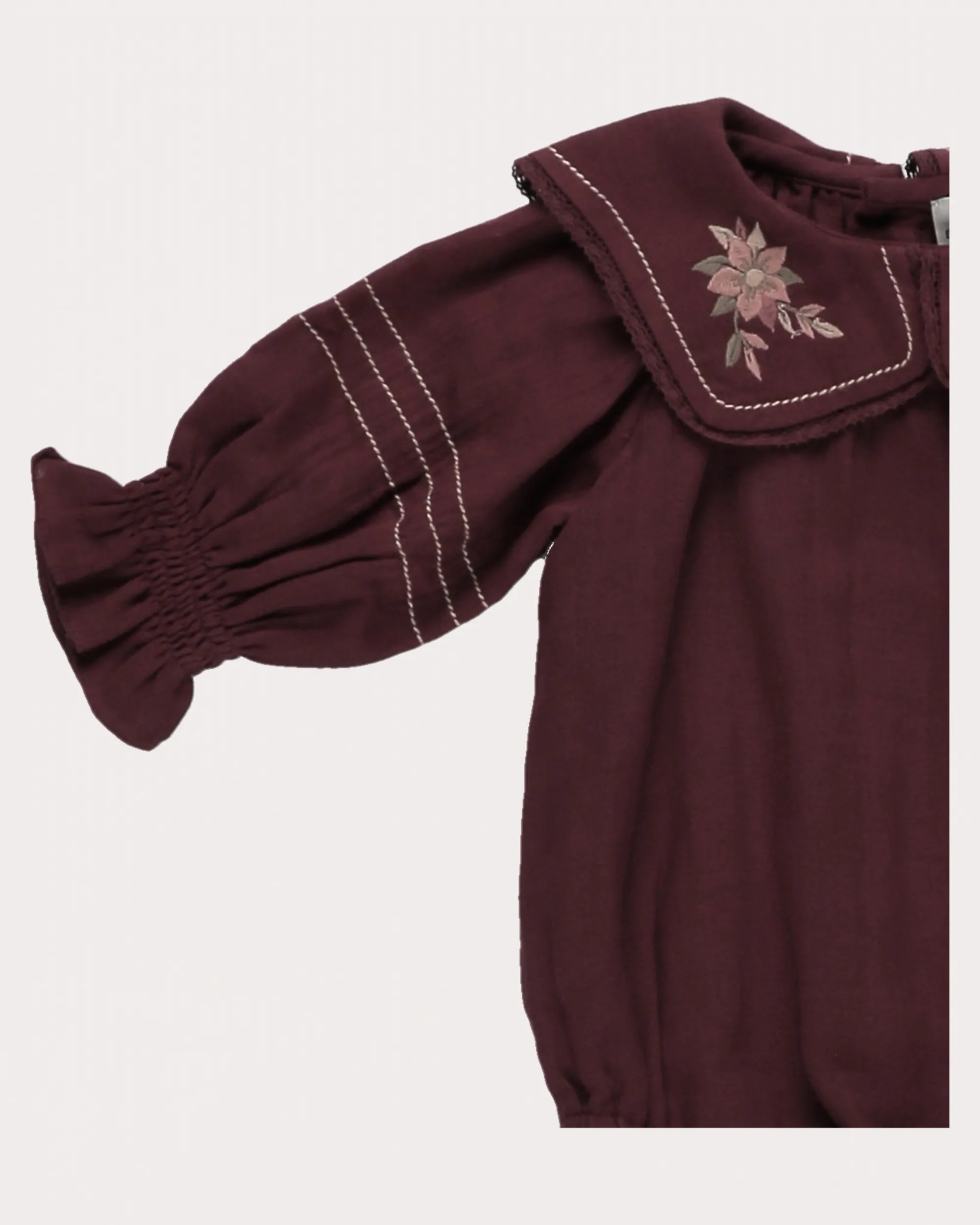 Early Sunday, Gladys Baby Bubble Romper in Plum, made from Cotton Double Gauze fabric, featuring a floral embroidered collar with beautiful lace yoke, shown in a closeup flat-lay view