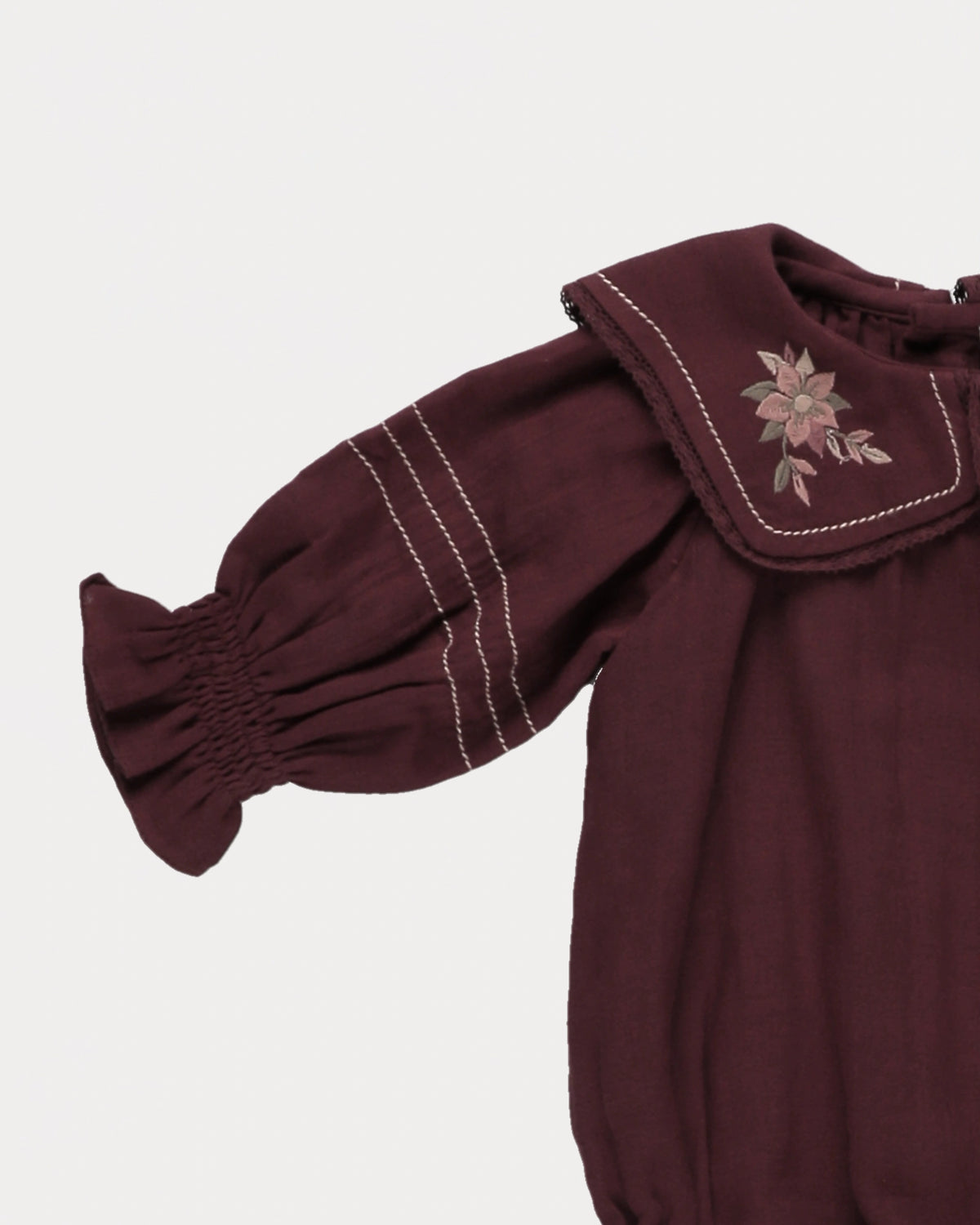 Early Sunday, Gladys Baby Bubble Romper in Plum, made from Cotton Double Gauze fabric, featuring a floral embroidered collar with beautiful lace yoke, shown in a closeup flat-lay view