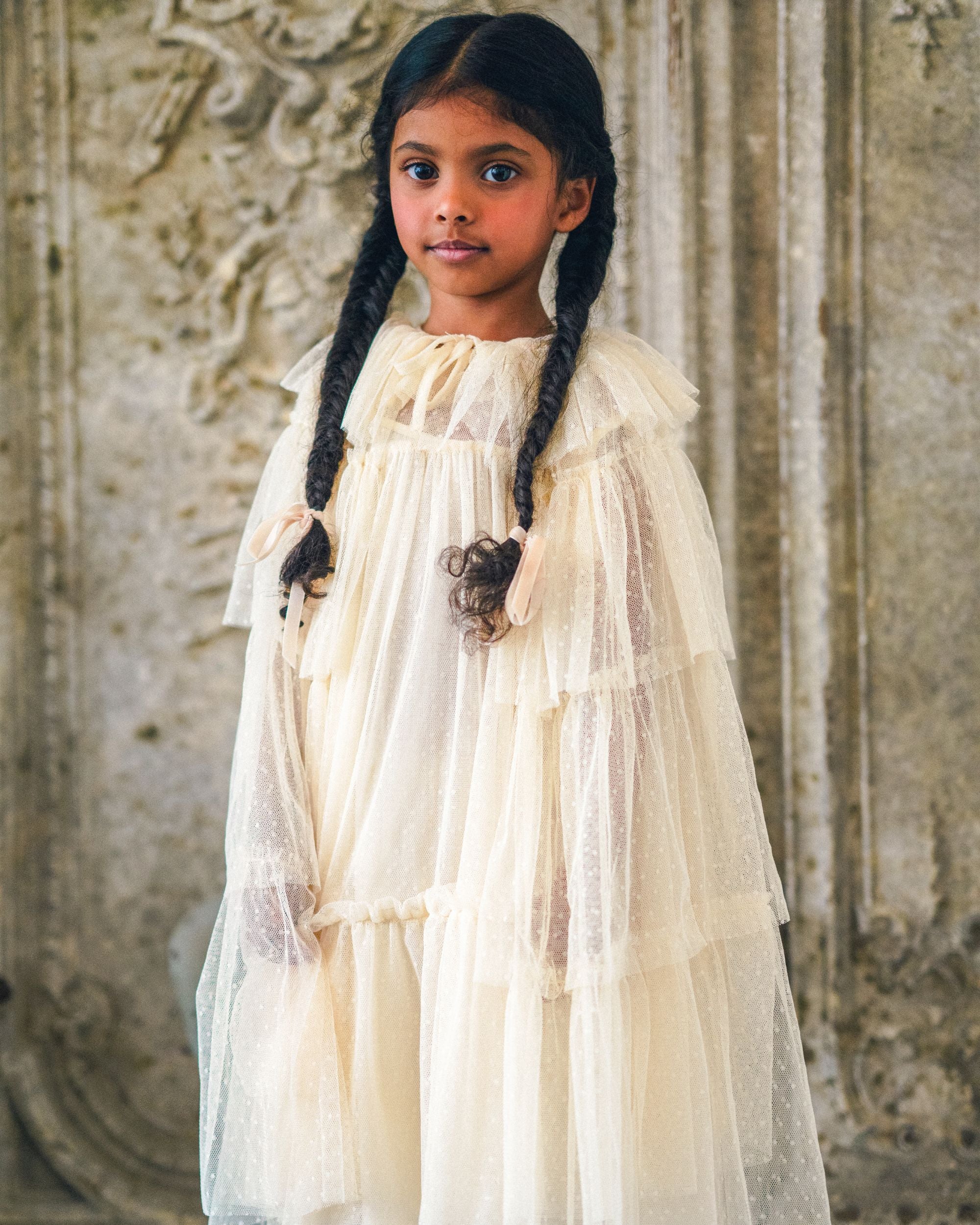 Early Sunday, Grace Cape in Hazelnut Cream, made from Dyed Nylon Mesh Dobby fabric, featuring Tiered ruffles create volume and whimsical movement, shown in a front view of a model wearing it in a studio setting