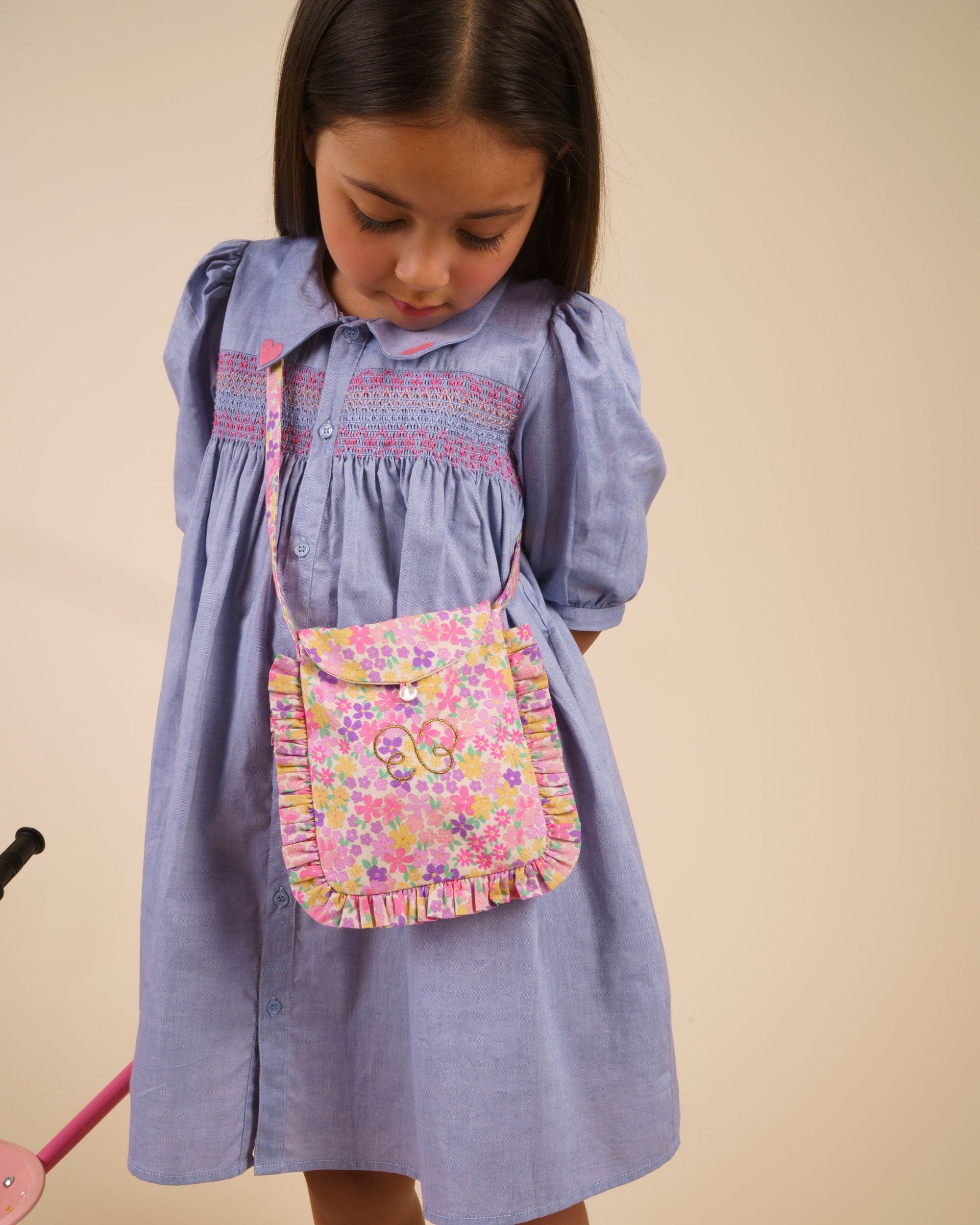 Early Sunday, Jane Dress in Summer Sky color, made from 100% cotton chambray fabric, featuring Smocked / embroidered yoke, peter pan collar and puffed short sleeves, shown in a Model side pose / slight angle