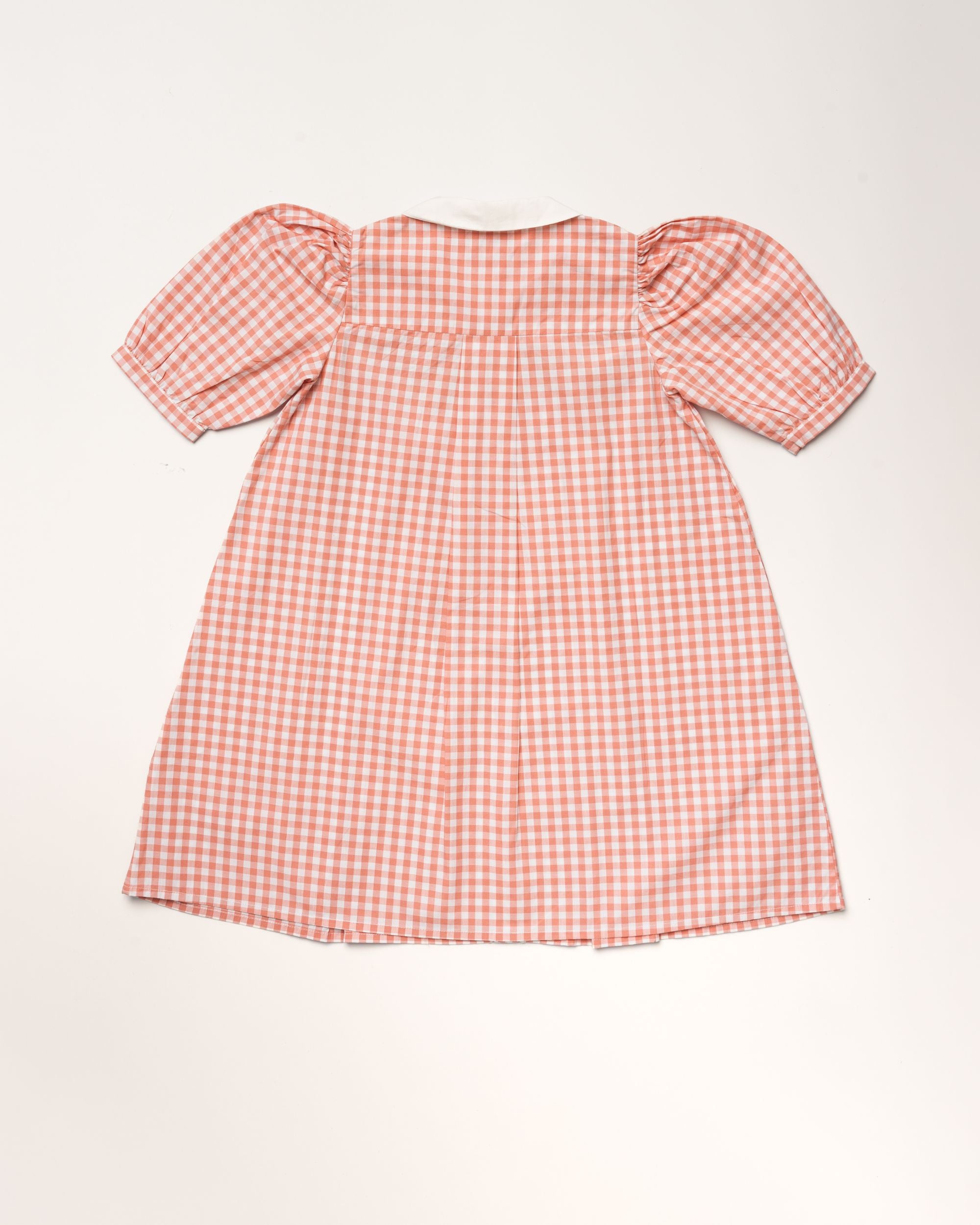 Early Sunday, Jane Dress in Peony color, made from 100% cotton gingham checks fabric, featuring Smocked / embroidered yoke, peter pan collar and puffed short sleeves, shown in a back flat-lay view