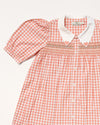 Early Sunday, Jane Dress in Peony color, made from 100% cotton gingham checks fabric, featuring Smocked / embroidered yoke, peter pan collar and puffed short sleeves, shown in a closeup flat-lay view