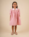 Early Sunday, Jane Dress in Peony color, made from 100% cotton gingham checks fabric, featuring Smocked / embroidered yoke, peter pan collar and puffed short sleeves, shown in a front view of model wearing