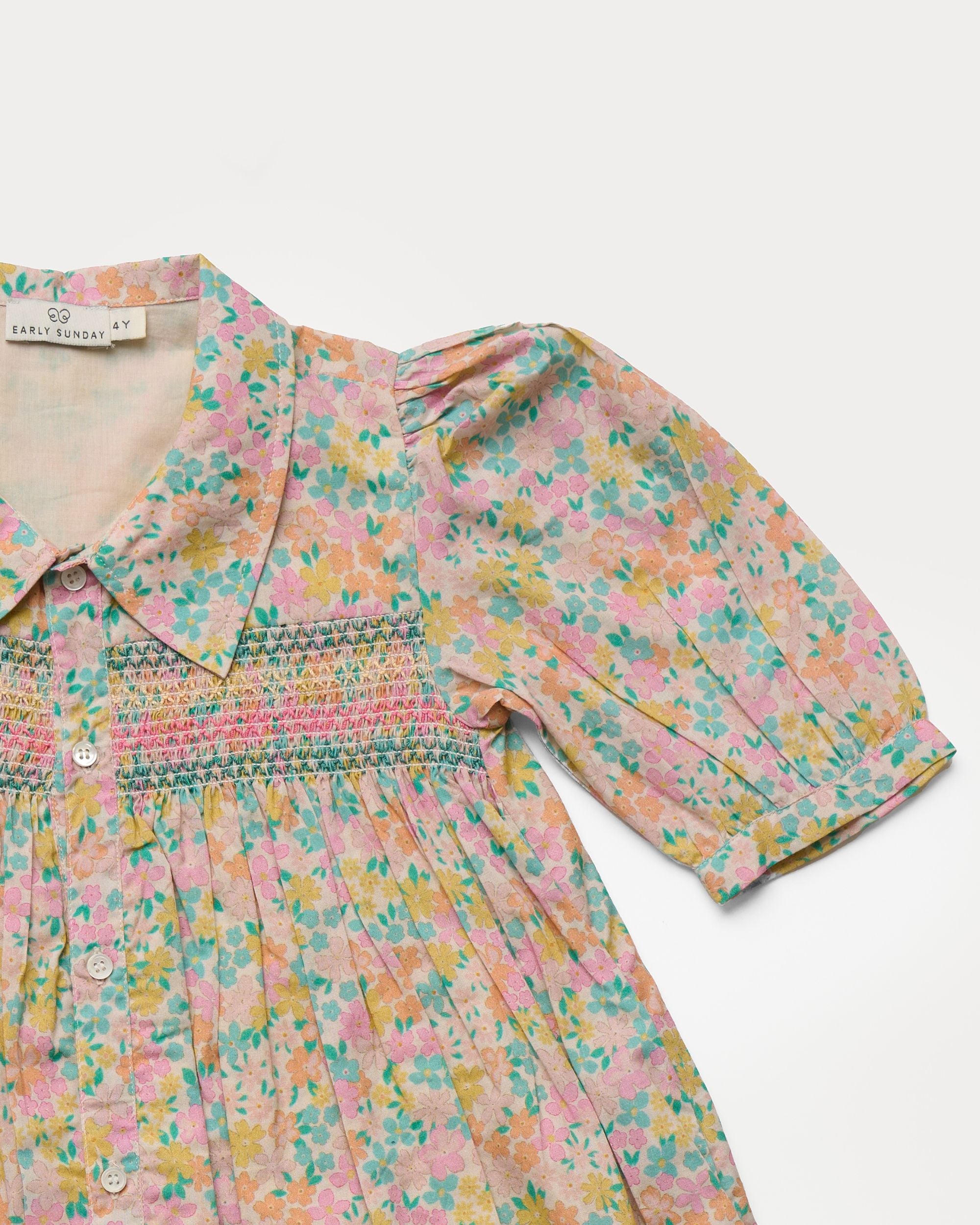 Early Sunday, Jane Dress in Emma Floral Mint color, made from printed 60s cotton cambric fabric, featuring Smocked / embroidered yoke, peter pan collar and puffed short sleeves, shown in a closeup flat-lay view