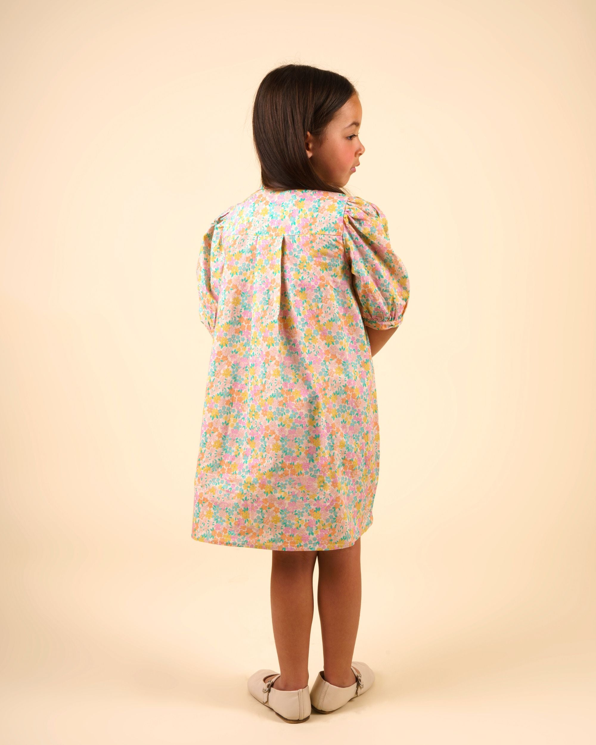 Early Sunday, Jane Dress in Emma Floral Mint color, made from printed 60s cotton cambric fabric, featuring Smocked / embroidered yoke, peter pan collar and puffed short sleeves, shown in a back view of model wearing