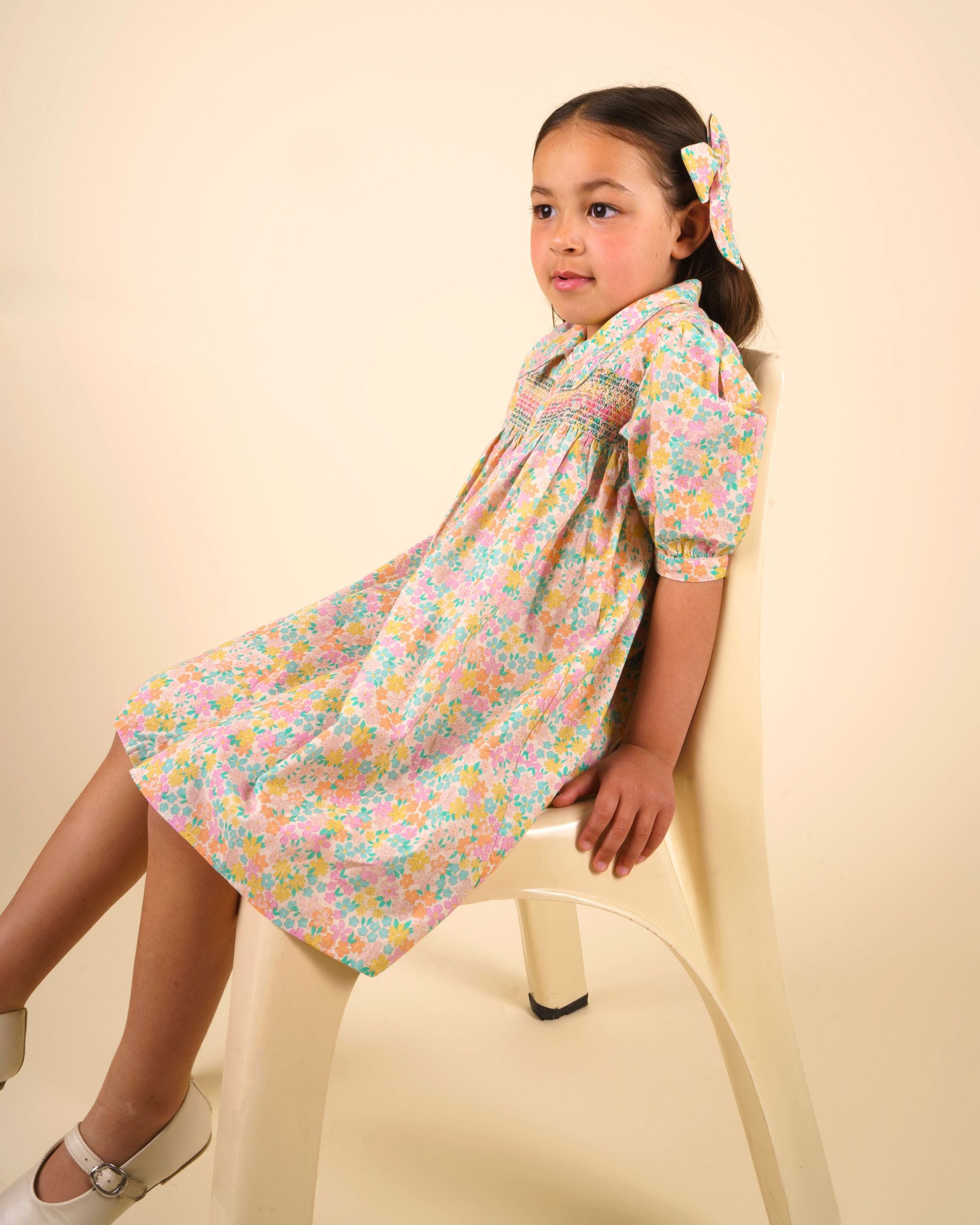 Early Sunday, Jane Dress in Emma Floral Mint color, made from printed 60s cotton cambric fabric, featuring Smocked / embroidered yoke, peter pan collar and puffed short sleeves, shown in a close up shot of model wearing it