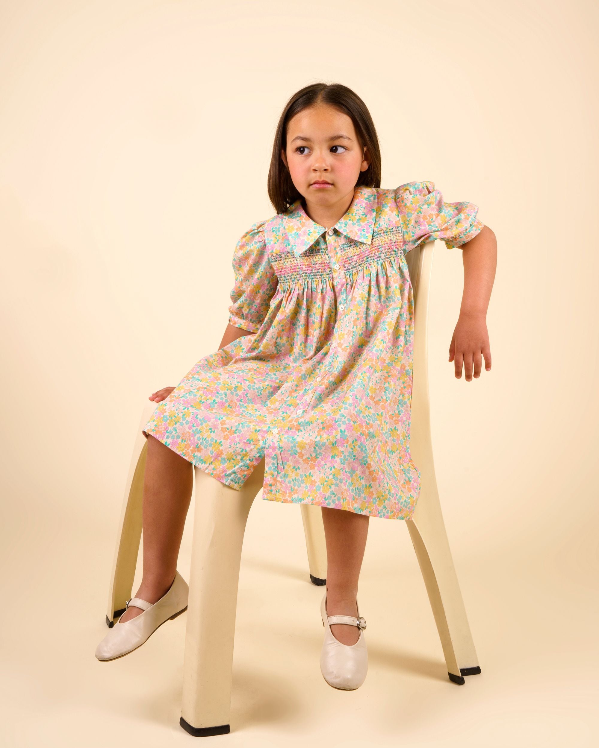 Early Sunday, Jane Dress in Emma Floral Mint color, made from printed 60s cotton cambric fabric, featuring Smocked / embroidered yoke, peter pan collar and puffed short sleeves, shown in a Model side pose / slight angle