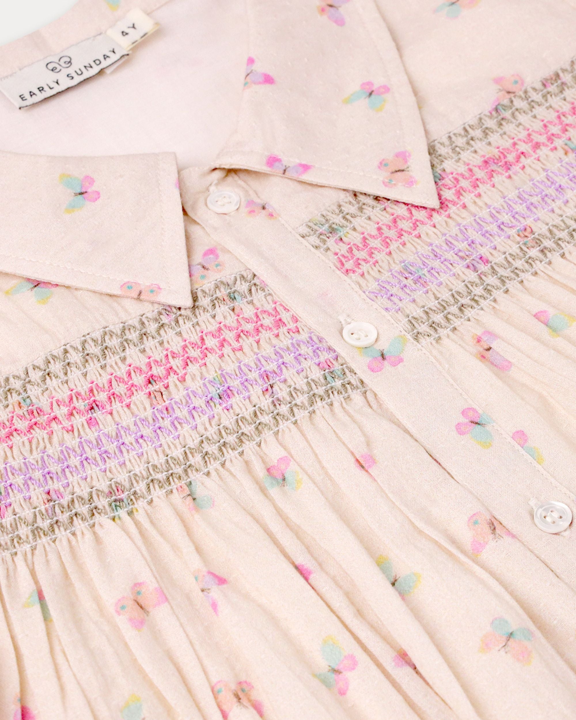 Early Sunday, Jane Dress in Butterfly Print color, made from printed cotton tiny swiss dobby fabric, featuring Smocked / embroidered yoke, peter pan collar and puffed short sleeves, shown in a closeup flat-lay view