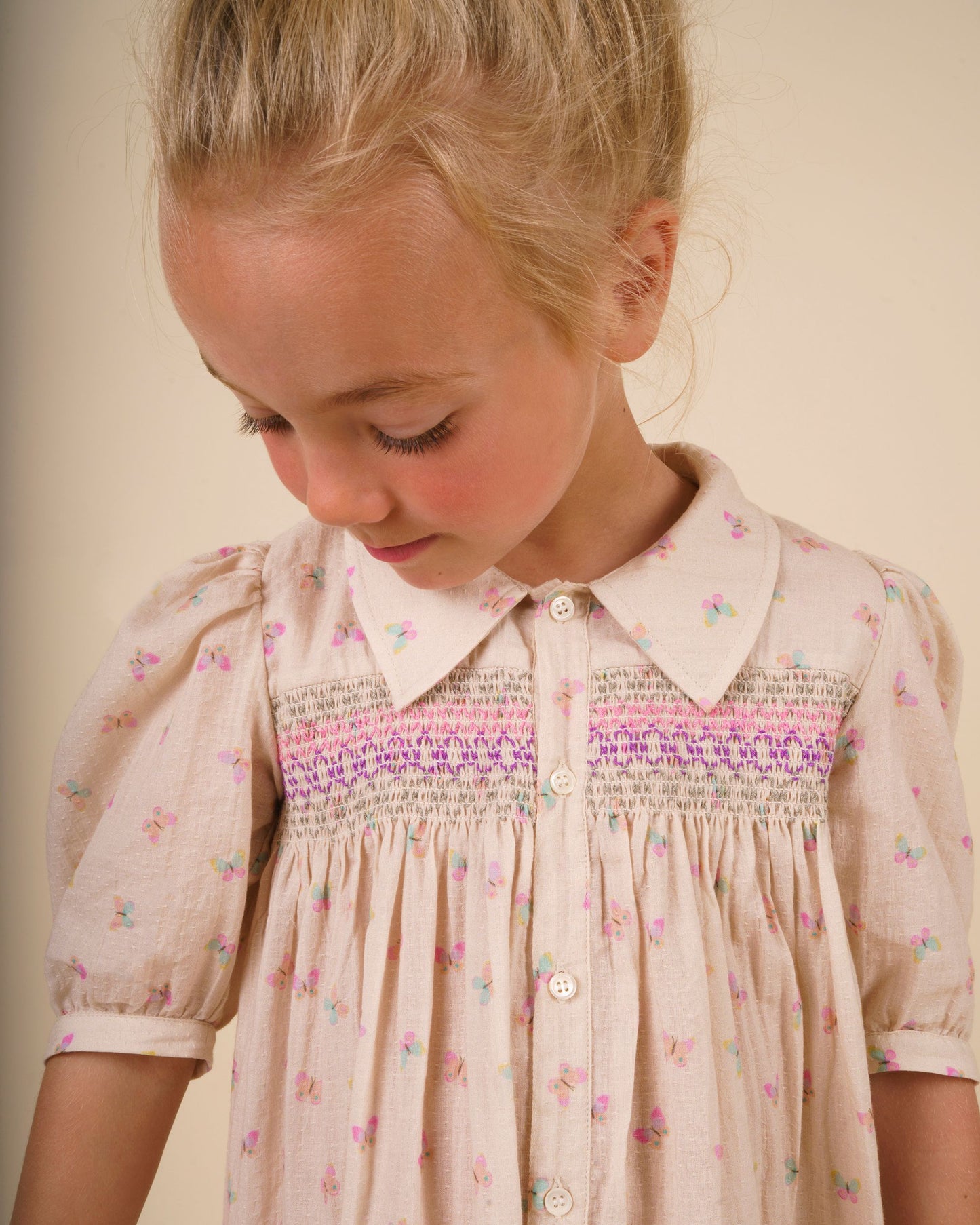 Early Sunday, Jane Dress in Butterfly Print color, made from printed cotton tiny swiss dobby fabric, featuring Smocked / embroidered yoke, peter pan collar and puffed short sleeves, shown in a close up shot of model wearing it