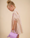 Early Sunday, Jane Dress in Butterfly Print color, made from printed cotton tiny swiss dobby fabric, featuring Smocked / embroidered yoke, peter pan collar and puffed short sleeves, shown in a side view of model wearing it